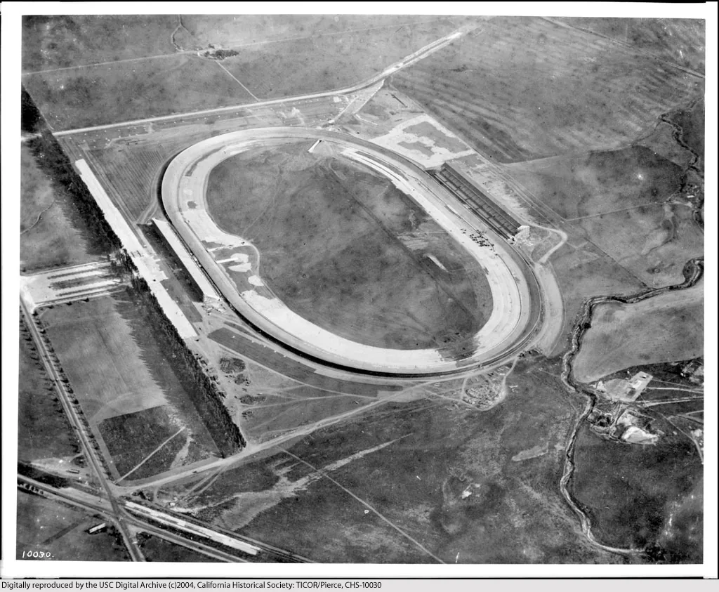 Archival aerial photograph: an oval board speedway surrounded by open land and a few roads